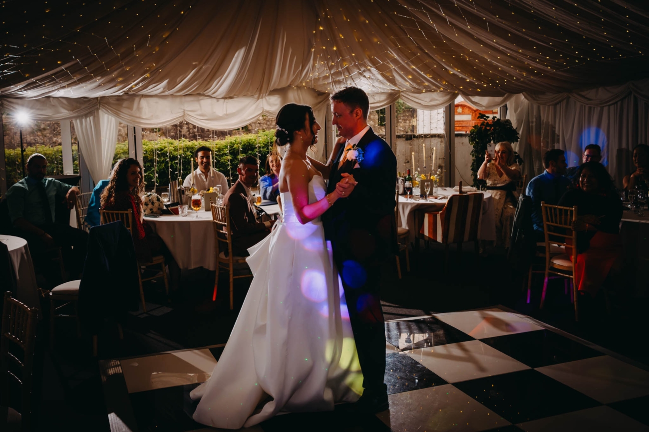Bride and groom sharing their first dance under coloured lights at the Old Post House in St Fagans
