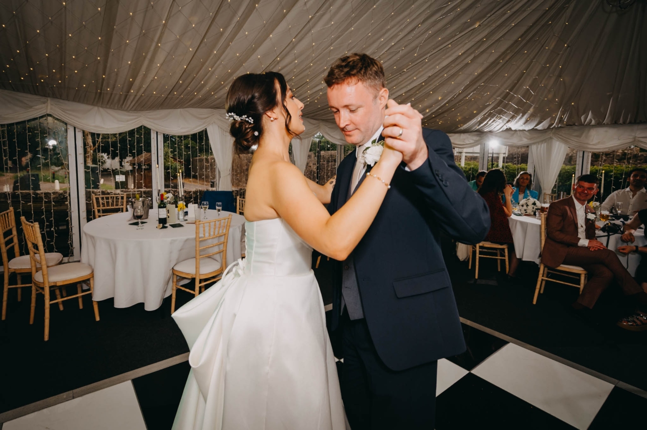 Bride and groom holding each other during their first dance inside the Old Post House marquee