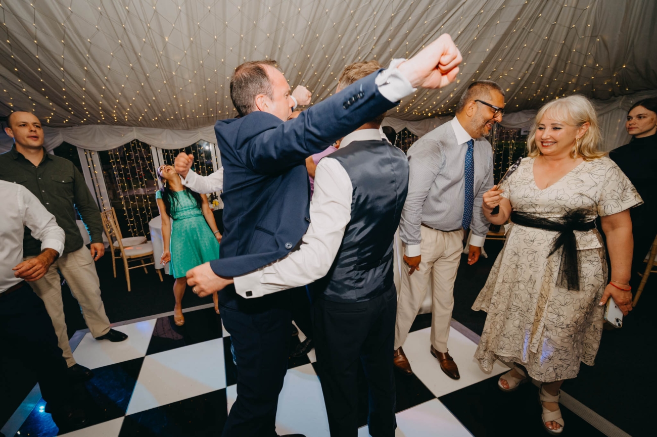 Wedding guests dancing together with their arms raised beneath the marquee lights