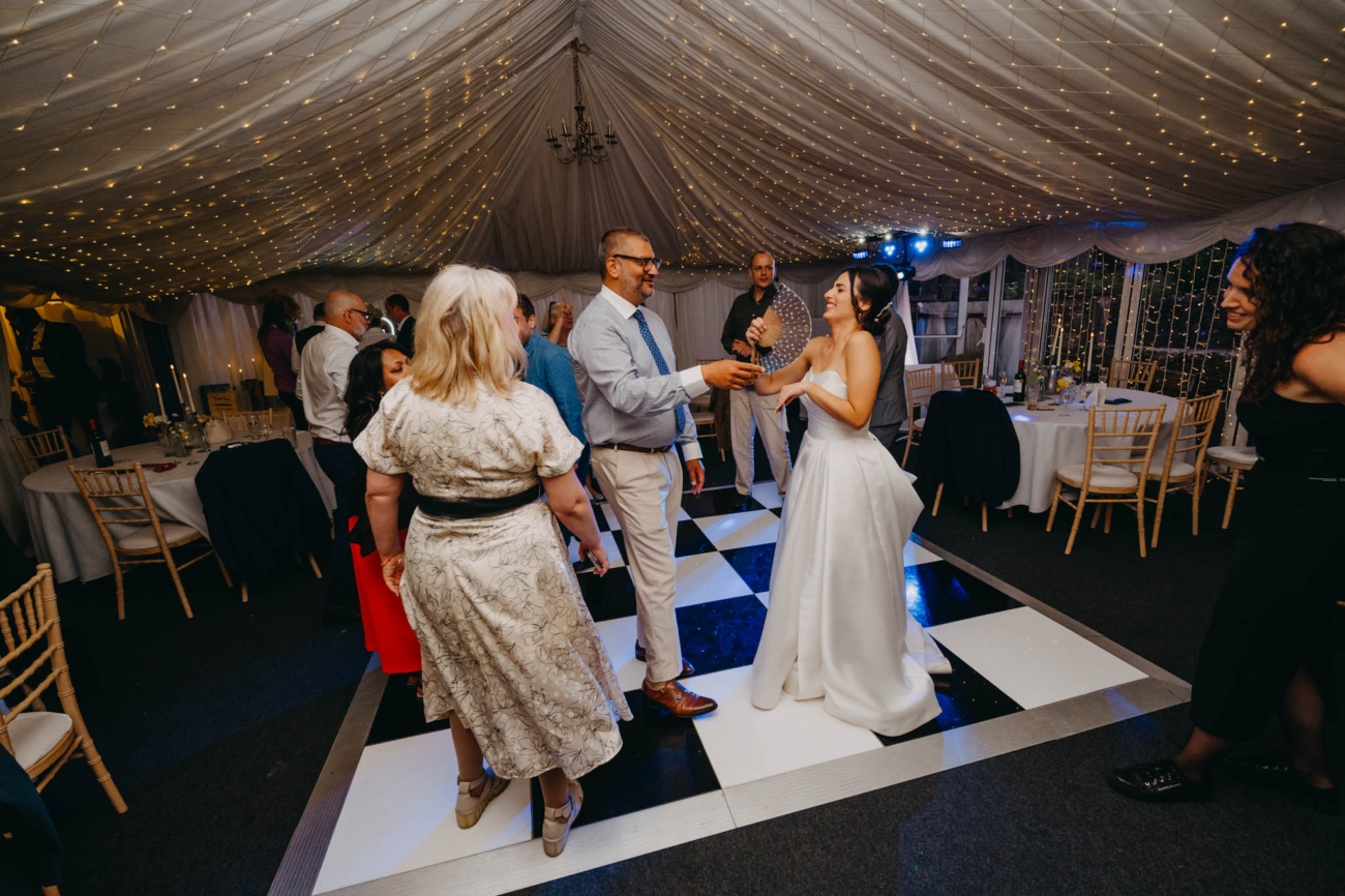 Bride and wedding guests dancing beneath fairy lights inside the Old Post House marquee