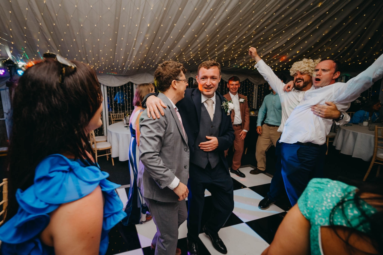 Groom surrounded by cheering wedding guests on the crowded dance floor