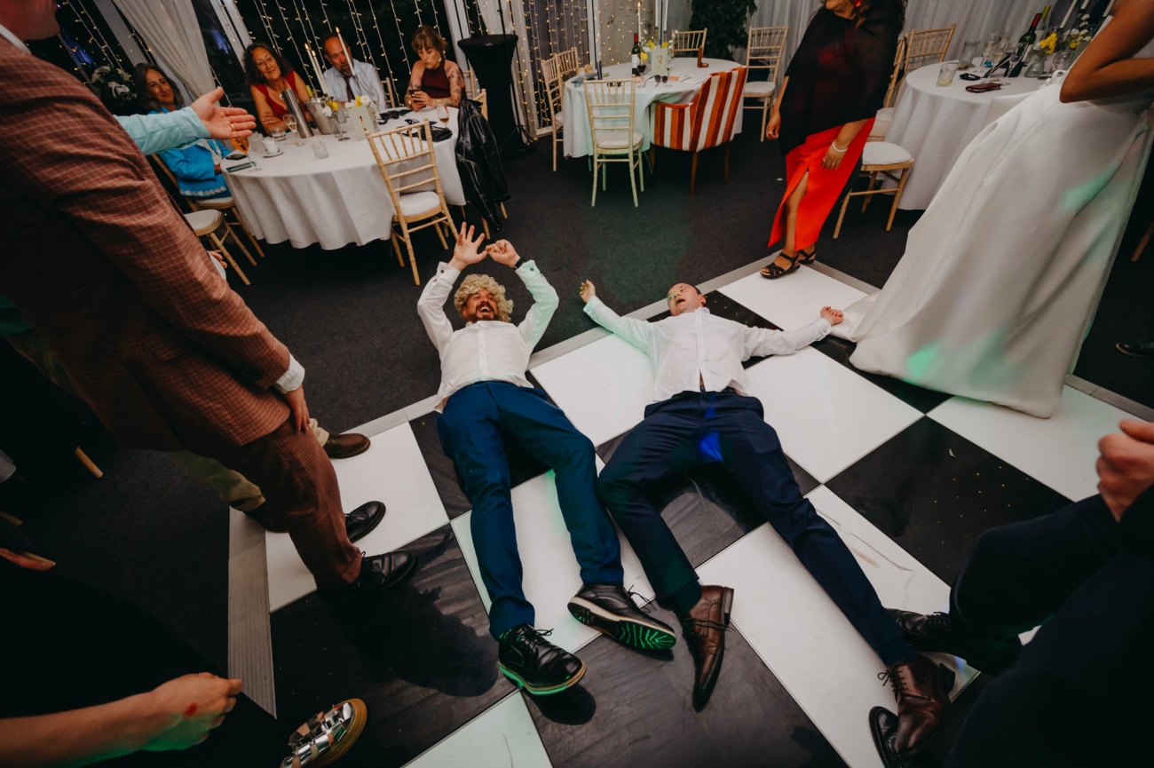 Two wedding guests lying on the chequered dance floor as the party continues around them