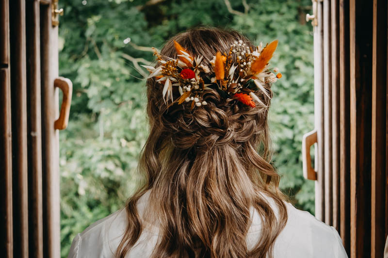 Bridal hairstyle with intricate braids and orange floral hair accessories, photographed from behind